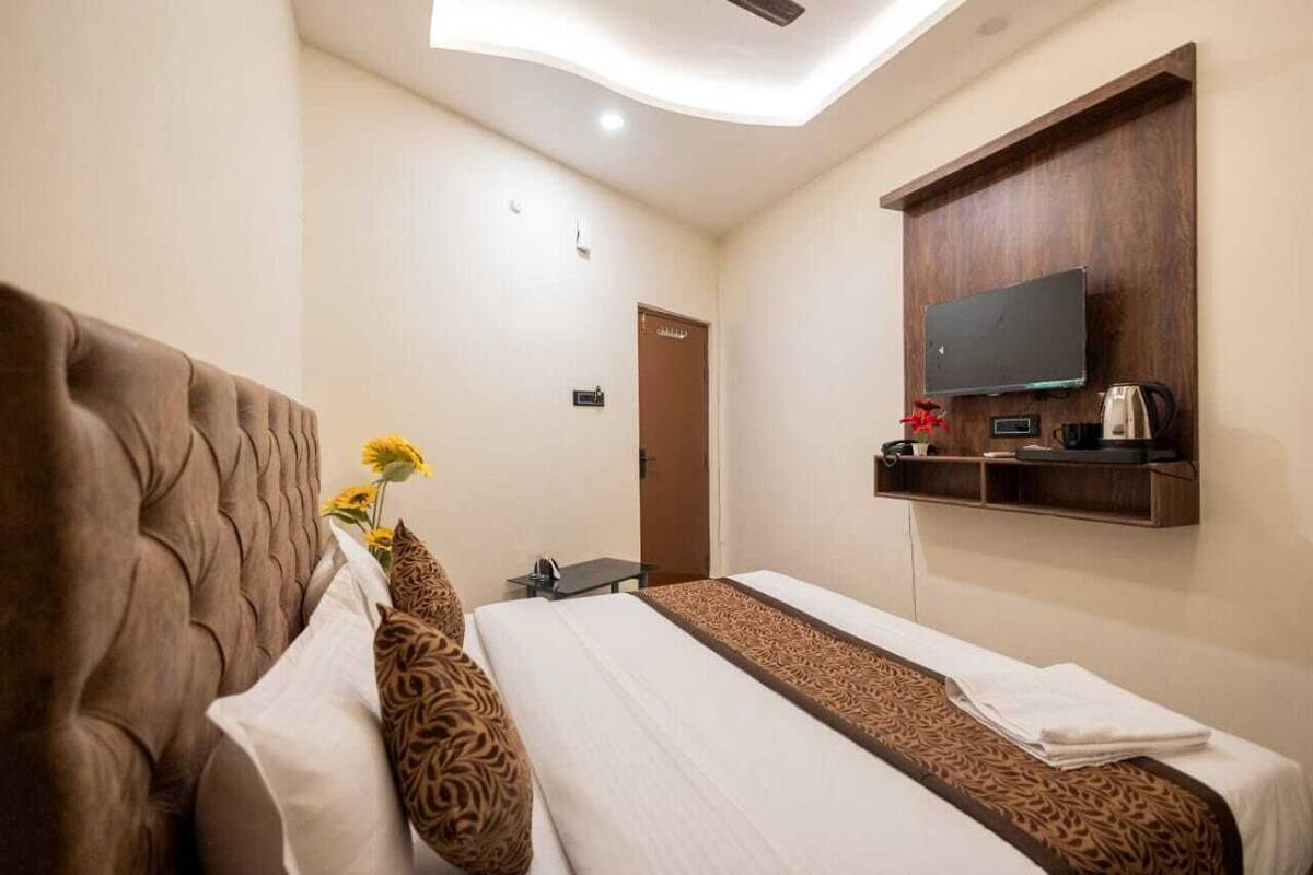 A hotel room with a large bed, a television mounted on a wooden panel, and a small table with a kettle.