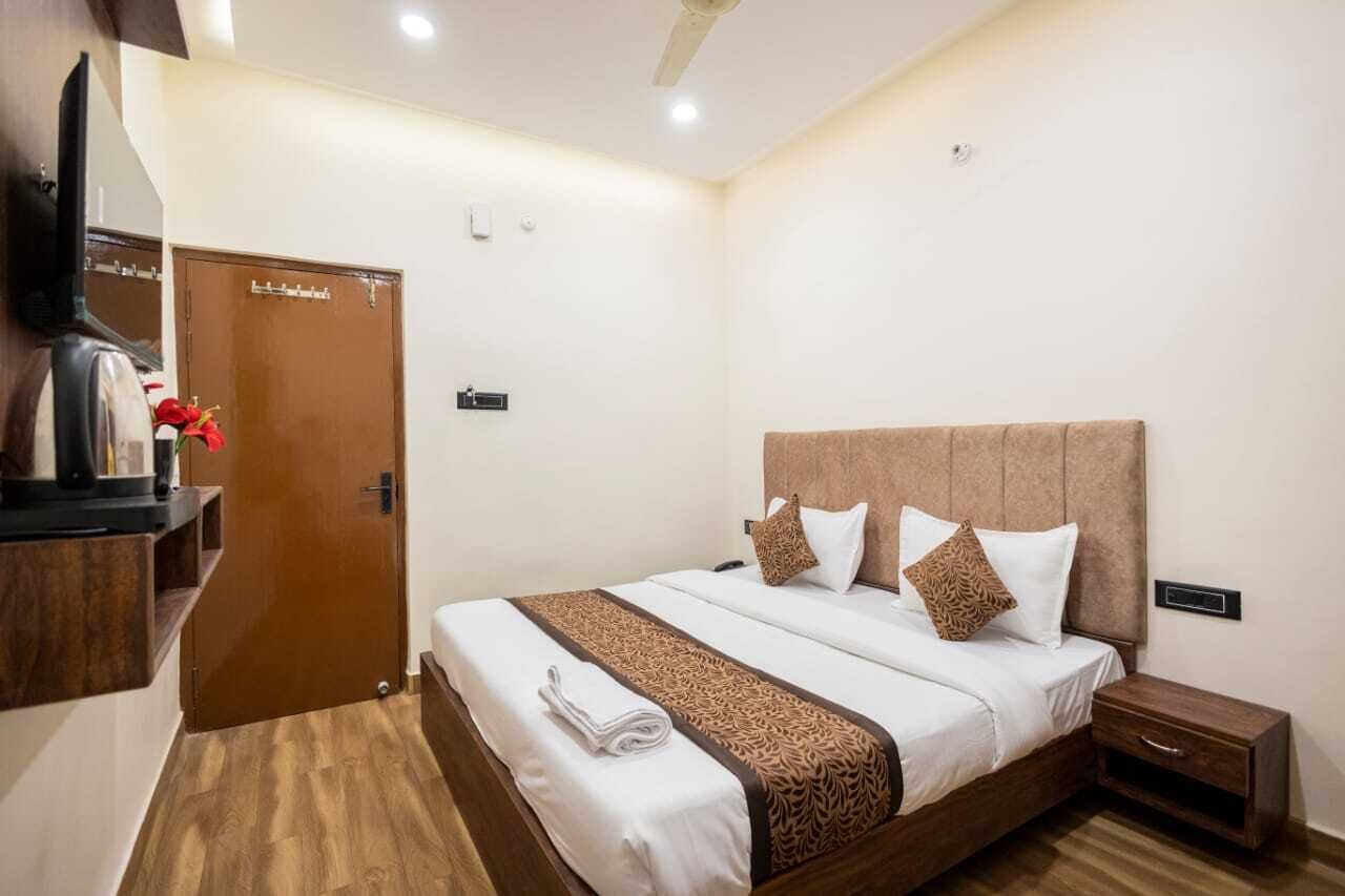 Habitación de hotel con una cama, una mesita de noche, un armario de madera, un televisor y una puerta.