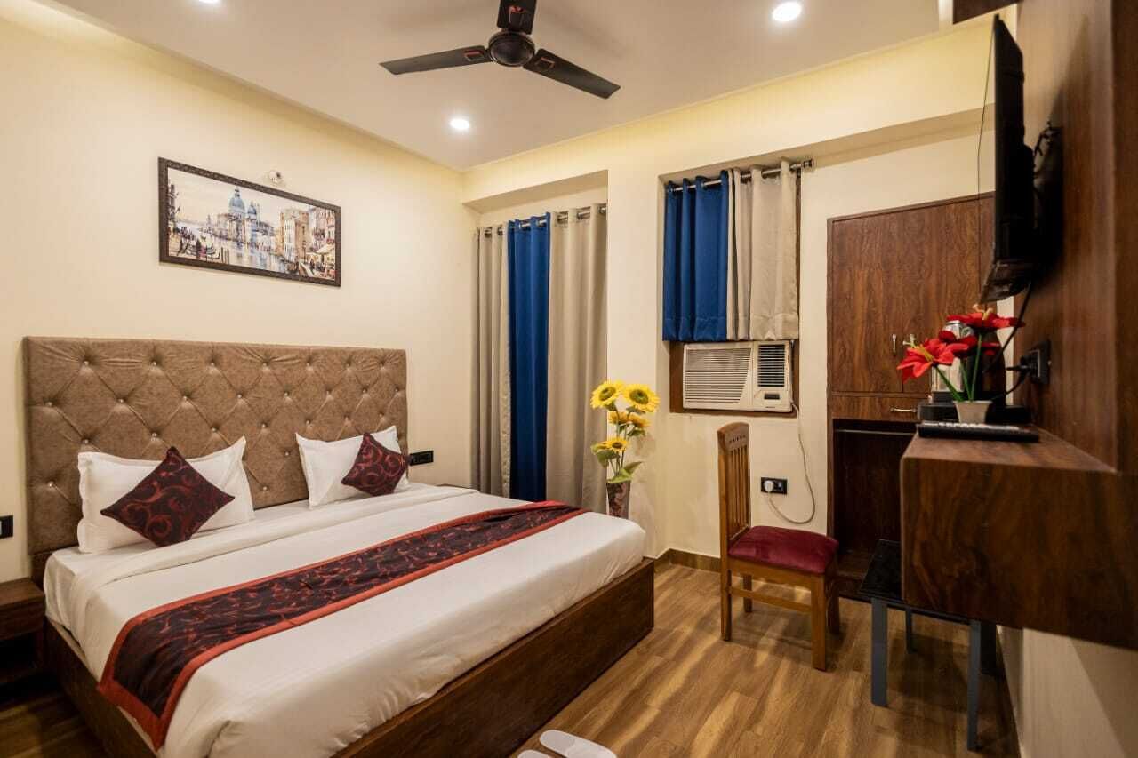 A hotel room with a large bed, a ceiling fan, a desk with a chair, a TV, and a window with curtains.