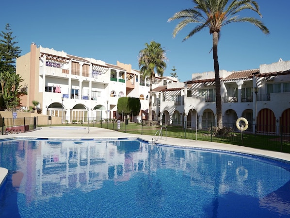 Ein Hotel mit Schwimmbad, mehreren Balkonen und Palmen.