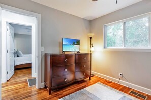 A bedroom with a wooden dresser, a bed, a window with a view, and a door leading to another room. - Hill House- Centrally Located, close to everything (Pensacola)