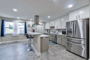 A modern kitchen with stainless steel appliances, a central island with bar stools, and a view of the outside. - Hill House- Centrally Located, close to everything (Pensacola)