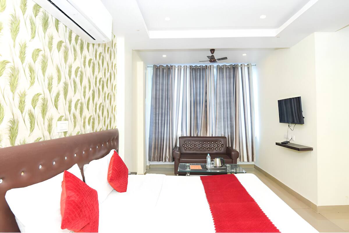 A modern hotel room with a large bed, a sofa, a TV, and a ceiling fan.