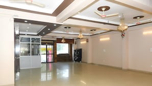 A spacious, well-lit room with a polished floor, ceiling fans, and a large window. - Hotel Moon Light Kanpur (Lucknow)