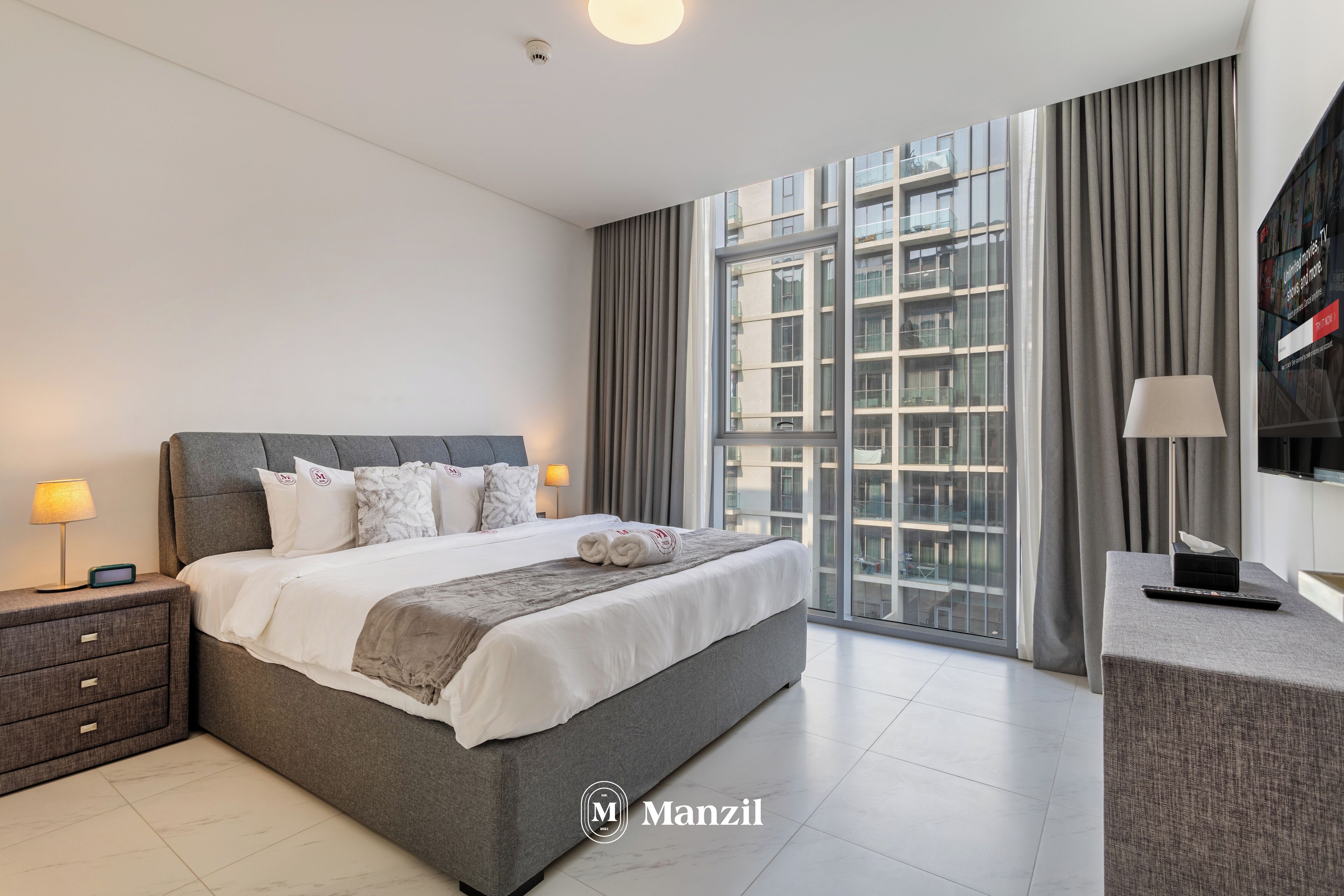 Quarto de hotel moderno com uma cama grande, uma escrivaninha e uma janela ampla com cortinas.