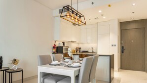 A modern dining area with a white table set for four, grey upholstered chairs, and a pendant light fixture above.