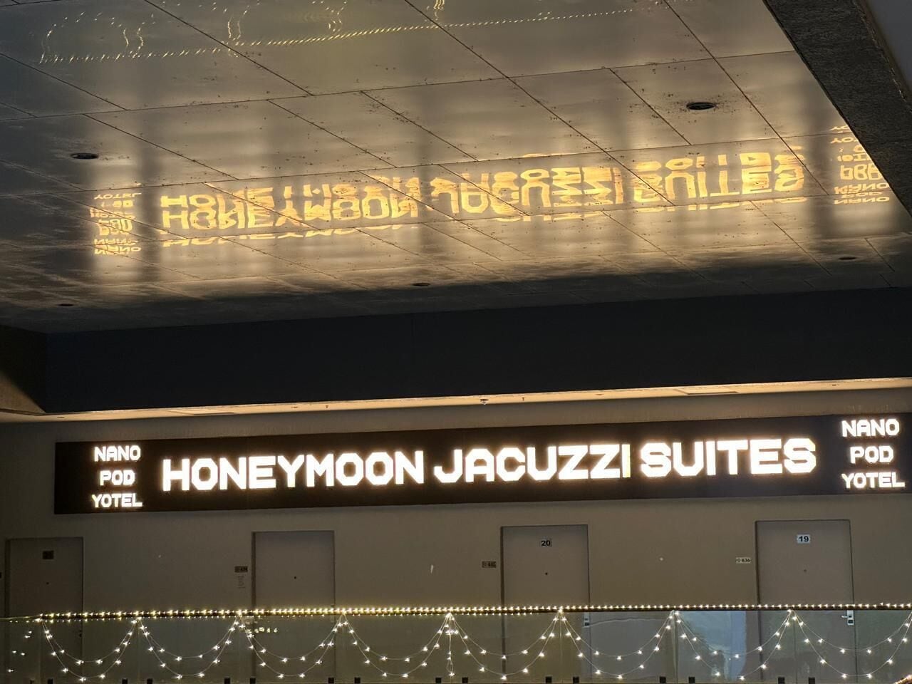 A hotel sign with neon lights spelling out "HONEYMOON JACUZZI SUITES" and "NANO POD YOTEL".