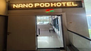 L'ingresso di un hotel con un neon che riporta 'NANO POD HOTEL' e un simbolo verde e rosso sopra di esso.