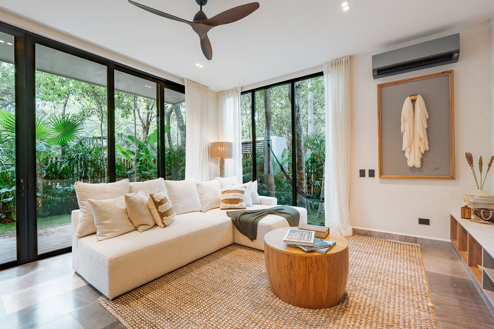 A modern living room with a large sectional sofa, a round wooden coffee table, and a view of lush greenery outside.
