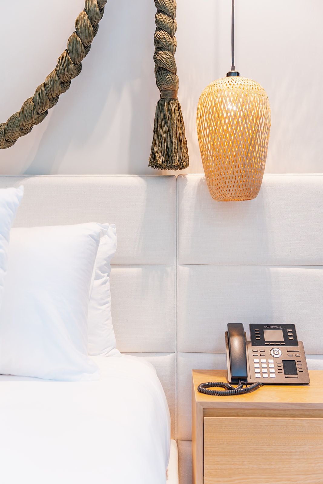 A hotel room with a bed, a bedside table with a telephone, and a wall-mounted lamp.