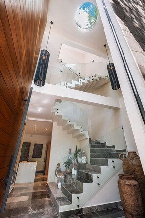 A modern interior with a staircase leading to a second floor, a glass railing, and a hanging light fixture. - Kachava Lux (Tulum)