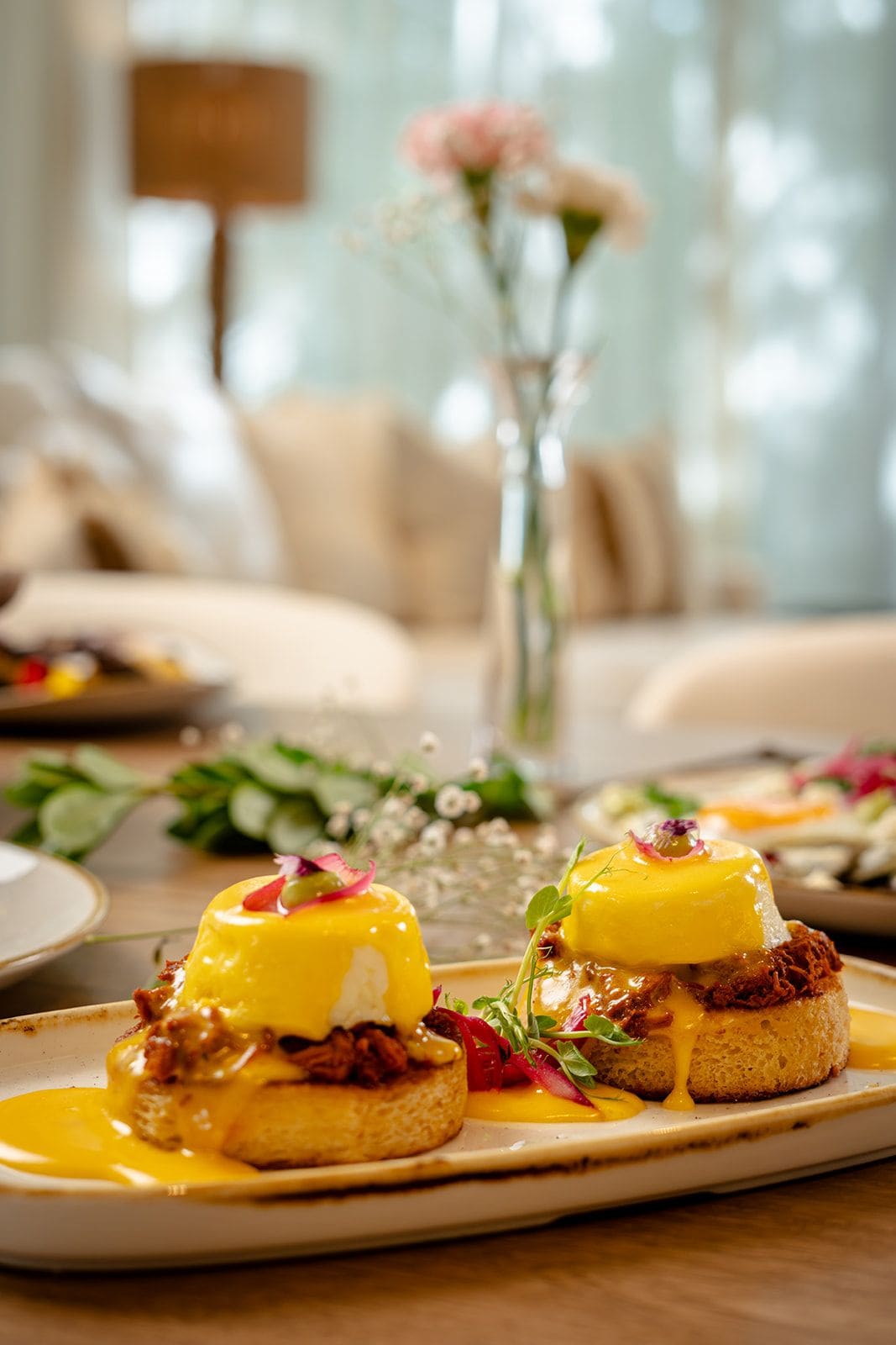 A breakfast setting with eggs benedict and a floral centerpiece.