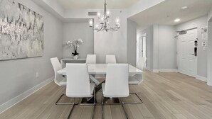 Un comedor moderno con una mesa y sillas blancas, una araña y un cuadro abstracto grande en la pared.