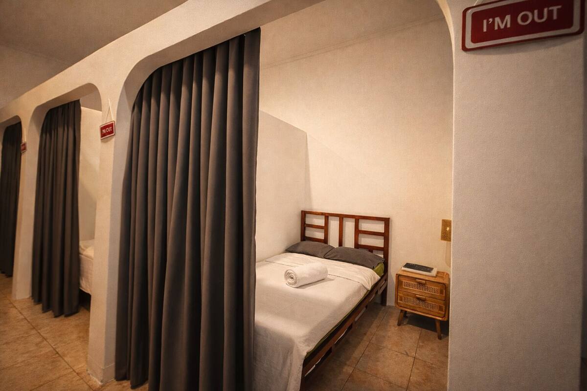 A hotel room with a bed, a nightstand, and a 'I'm out' sign on the wall.