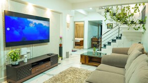 Ein modernes Wohnzimmer mit Fernseher, Sofa, Couchtisch und einer Treppe, die in eine weitere Ebene führt.