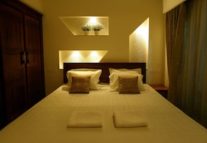 A hotel room with a large bed, two bedside tables, a wooden wardrobe, and a wall-mounted light fixture with two potted plants.
