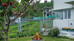 Un giardino con un fuoco, un'area recintata con piante e un edificio sullo sfondo.