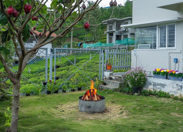 A garden with a fire pit, a fenced area with plants, and a building in the background.