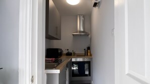 A narrow kitchen with a microwave, toaster, and oven. - Donnington Apartments - Studio 5 (Telford and Wrekin)