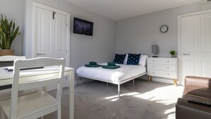 A bedroom with a bed, a desk, a chair, a dresser, a clock, and a plant. - Donnington Apartments - Studio 5 (Telford and Wrekin)