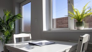 A room with a white table, two chairs, a potted plant, and a window with a view of a building. - Donnington Apartments - Studio 5 (Telford and Wrekin)