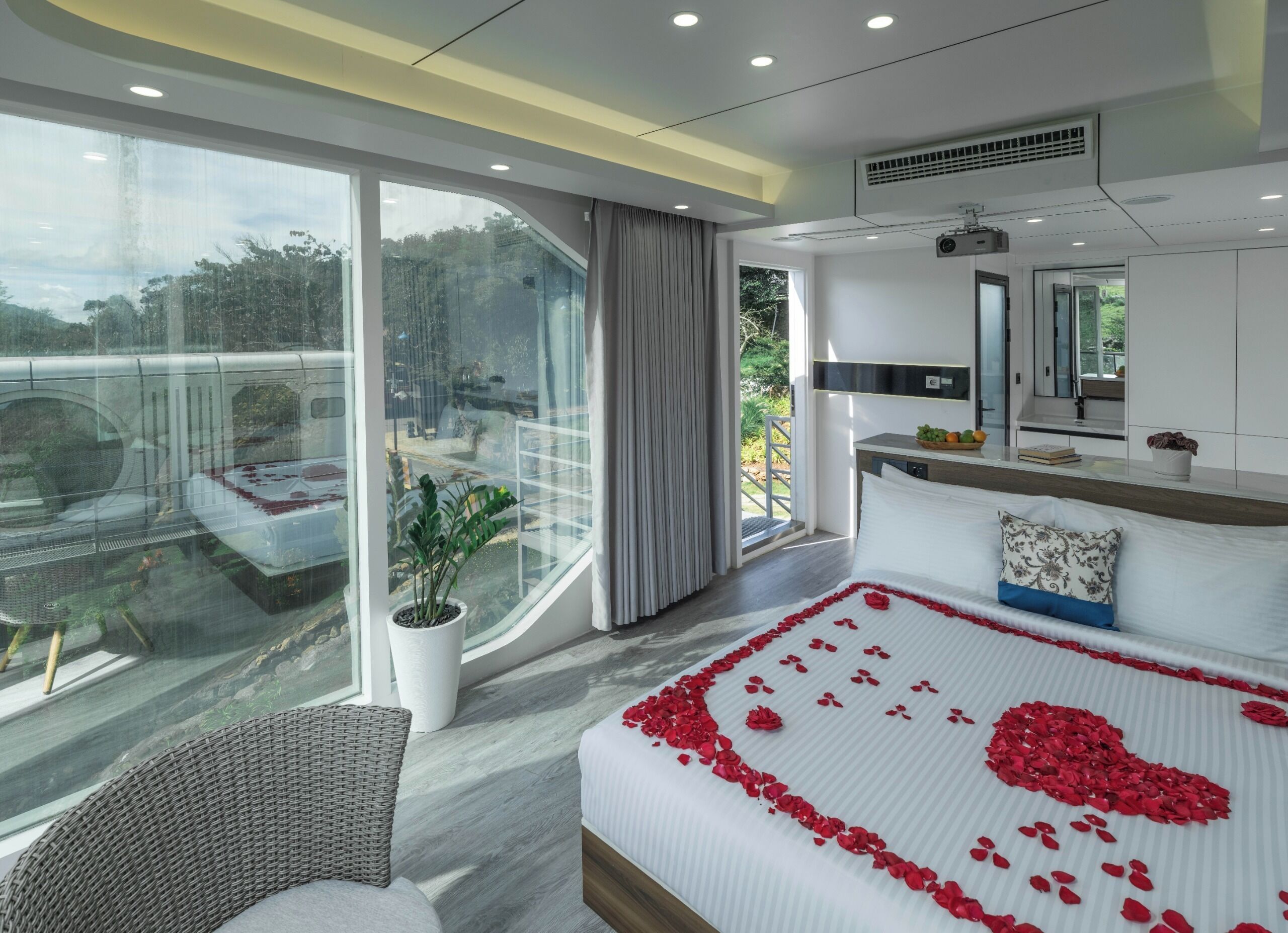 A modern hotel room with a large bed, a view of a balcony, and a dining area.
