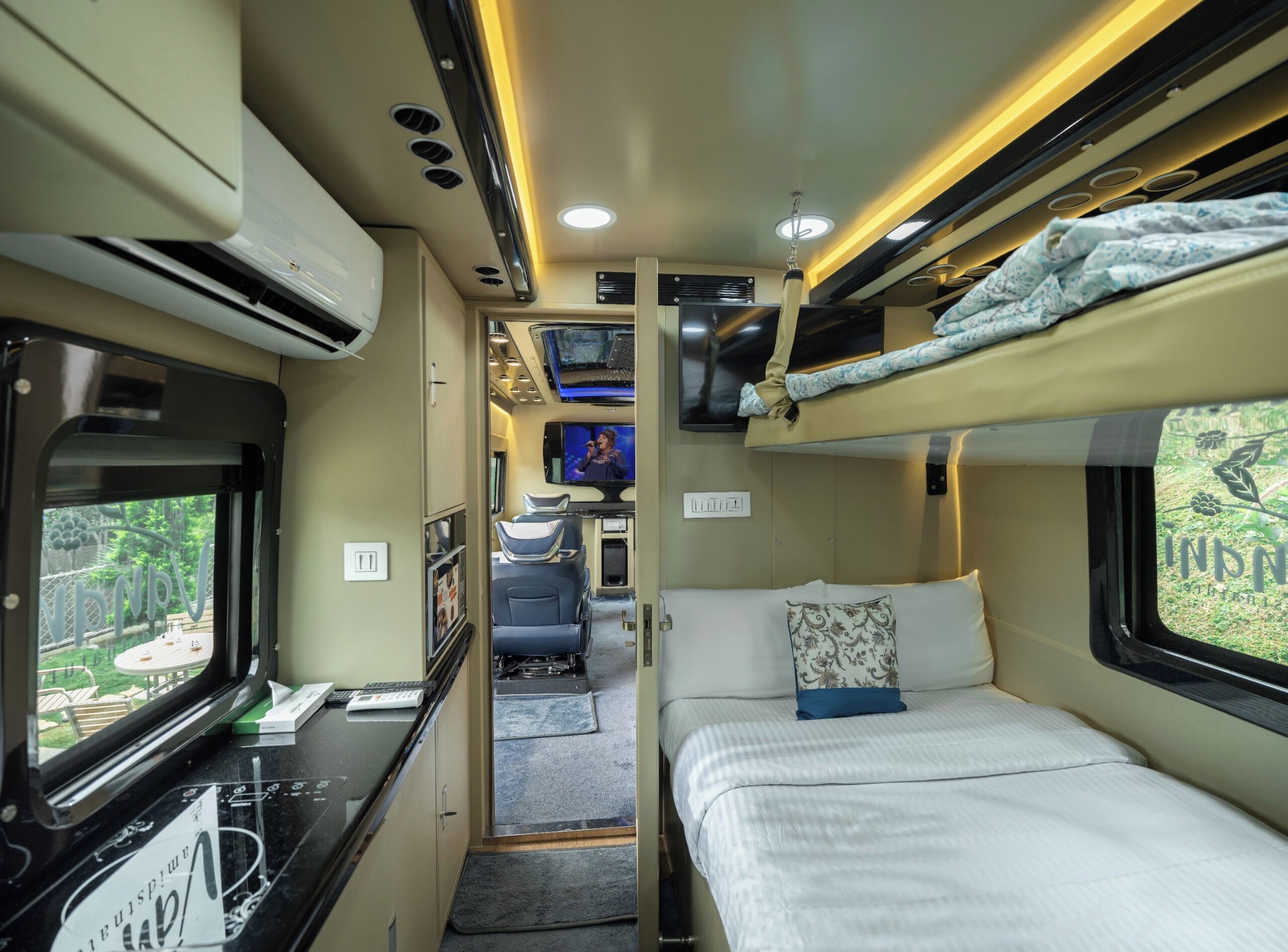 A compact train compartment with a bunk bed, a small desk with a laptop, and a TV screen.