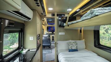 A compact train compartment with a bunk bed, a small desk with a laptop, and a TV screen.