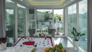 A modern room with large windows, a glass door leading outside, wicker furniture, a table with a flower arrangement, and a potted plant. - Vanani Resort and Caravan Park Munnar (Udumbanchola)