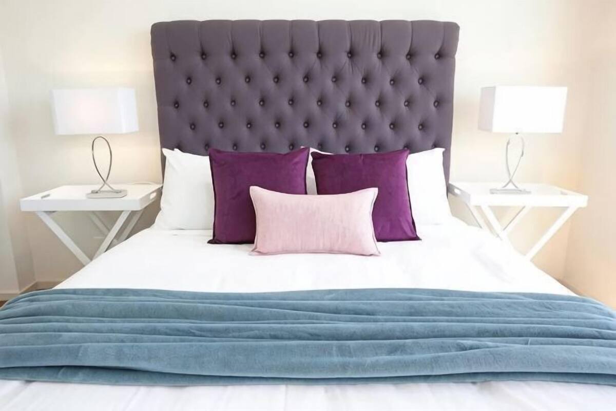 A bed with a tufted headboard, two bedside tables with lamps, and a blue throw blanket.