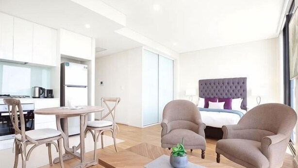 Een moderne hotelkamer met een zithoek, een bed met een gestapeld hoofdeinde en twee fauteuils.