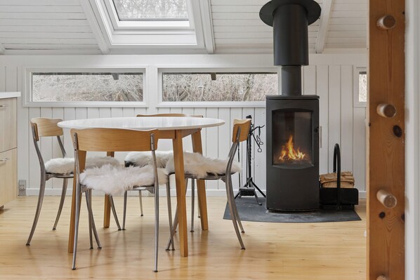 Een gezellige kamer met een ronde houten tafel, vier stoelen, een witte bontdrap en een houtkachel.