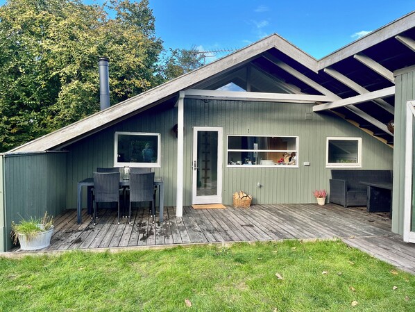 Een woonhuis met een overdekt terras, een eethoek met stoelen en een tafel, en uitzicht op de omgeving.