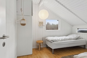A bedroom with a bed, a window, a hanging light fixture, and a door. - Charming cottage near the water (Holbæk)