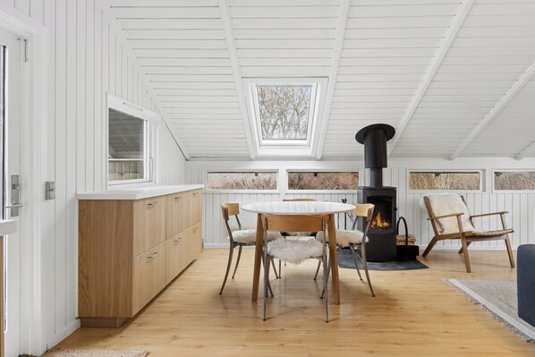 A modern kitchen with wooden cabinets, a round dining table, and a built-in wood stove. - Charming cottage near the water (Holbæk)