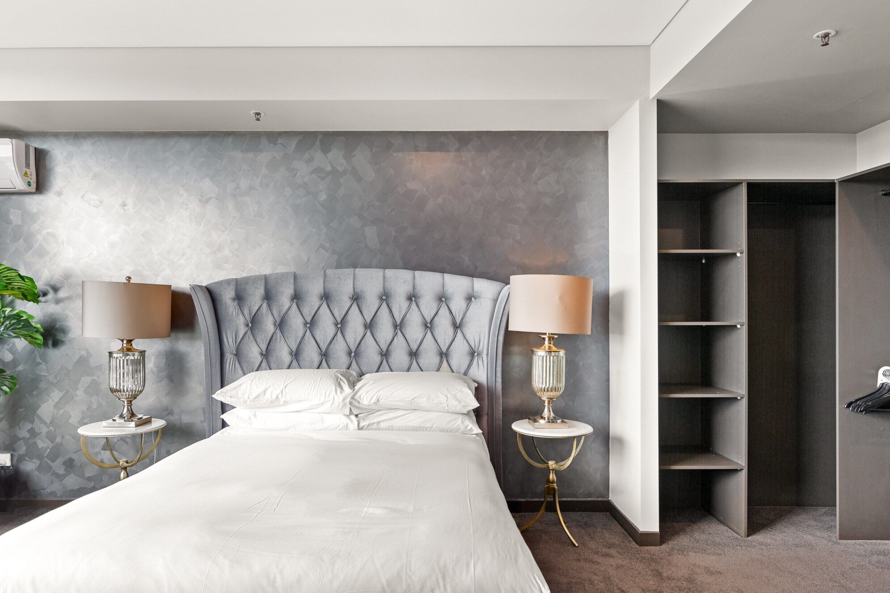 Un dormitorio moderno con cabecera capitonada, cama grande con ropa de cama blanca, dos mesitas de noche con lámparas y un armario empotrado.