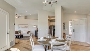 Zona pranzo con tavolo rotondo apparecchiato per quattro persone, circondato da sedie bianche. Sullo sfondo, una cucina con elettrodomestici moderni.