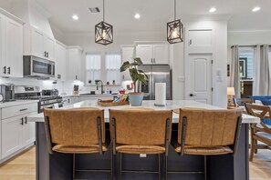 Cozinha moderna com armários brancos, eletrodomésticos de aço inoxidável e uma ilha central com banquetas.