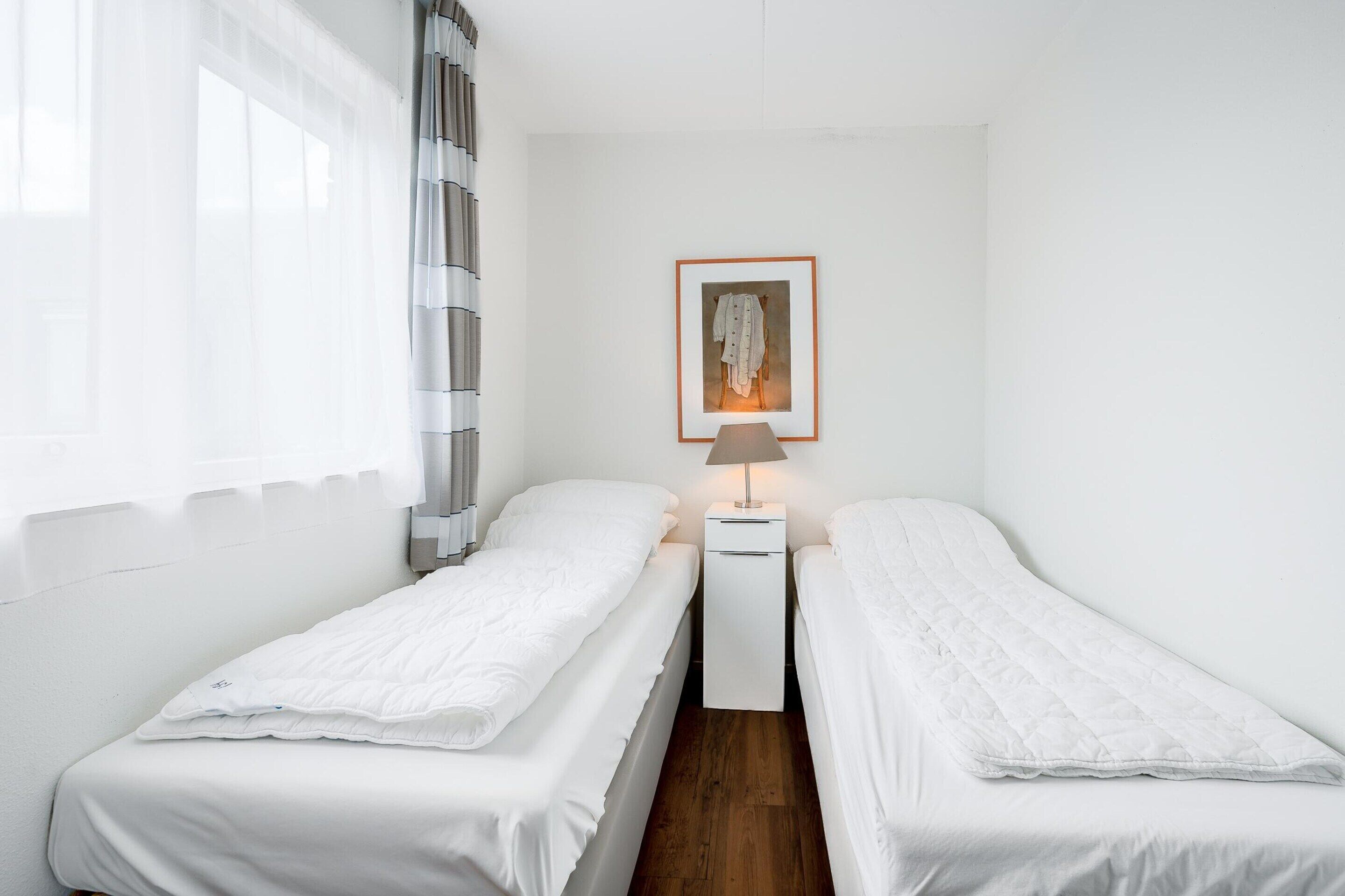 A small, clean room with two single beds, a bedside table with a lamp, and a framed picture on the wall.