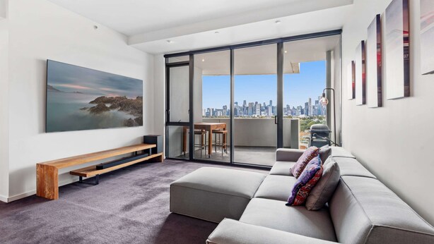 A modern living room with a large window, a sofa, a bench, and a painting. - 2-bed, 500m From The Beach With Pool, Gym & Sauna (Melbourne)