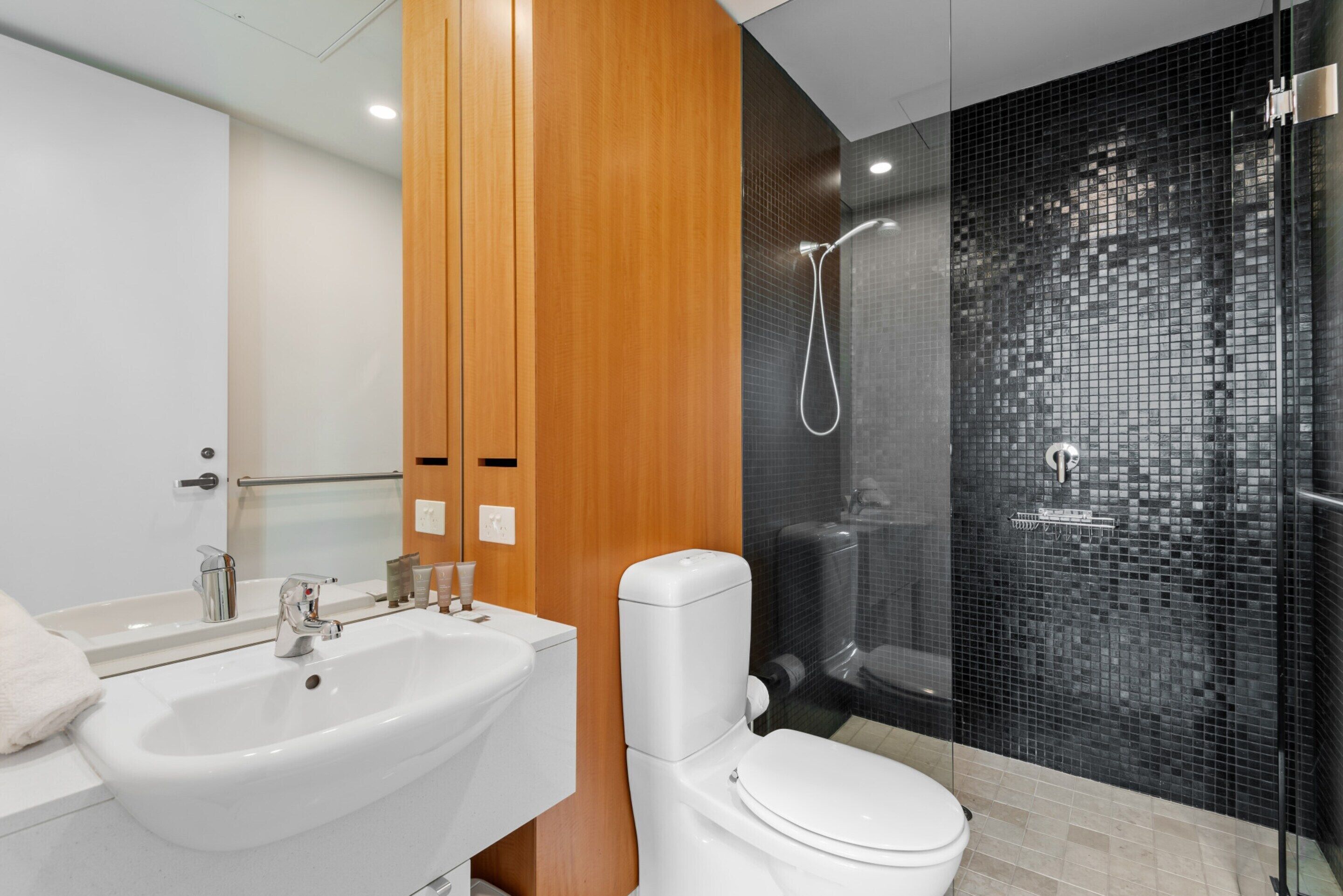 A modern bathroom with a white sink, a toilet, and a glass-enclosed shower area.