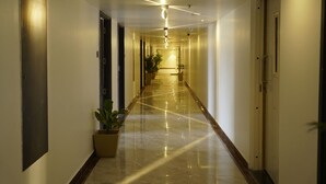 A long, well-lit hallway with a polished floor, doors on both sides, and potted plants along the corridor. - A79 by Khotels (Chennai)