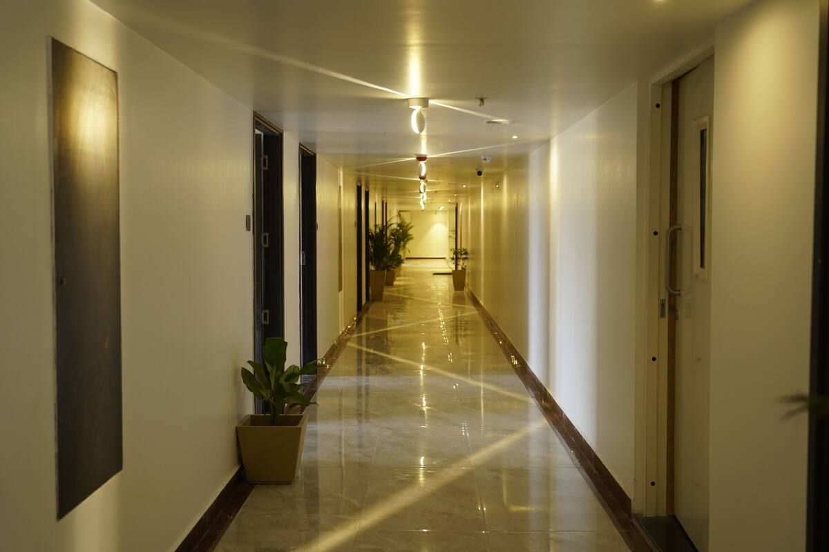 Un lungo corridoio ben illuminato con pavimento lucido, porte su entrambi i lati e piante in vaso lungo il percorso.