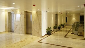 A modern hotel lobby with marble flooring, elevators, potted plants, and a glass railing. - A79 by Khotels (Chennai)