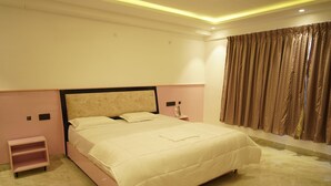 A bedroom with a large bed, a nightstand, a small shelf, and a window with curtains. - A79 by Khotels (Chennai)