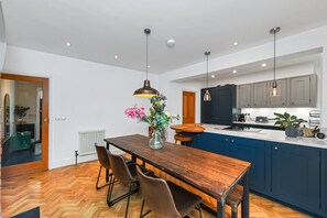 A modern kitchen with a wooden dining table, blue cabinets, and pendant lighting.