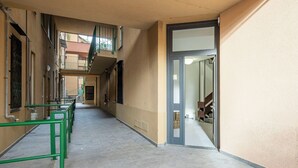 Un pasillo con piso de baldosas, barandas verdes y una puerta que da a una habitación con cama y ventana.