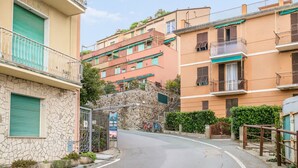 Una calle residencial con edificios de varios pisos, un muro de piedra y una entrada con portón.