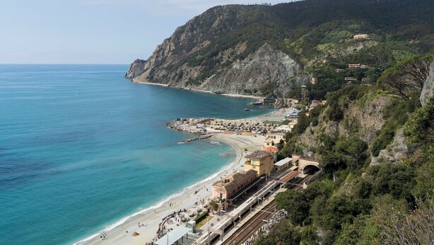 Un pueblo costero con una playa, una estación de tren y edificios en una colina.