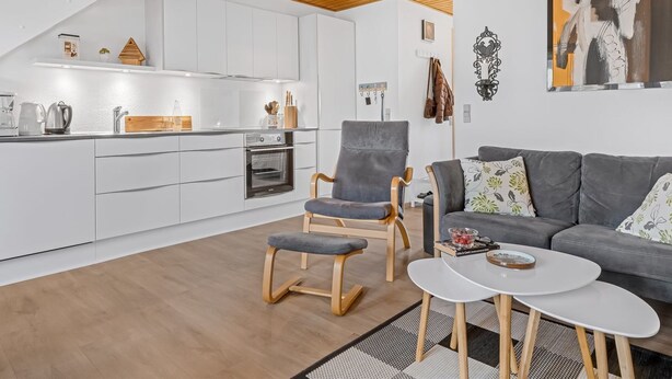 A modern kitchen with white cabinetry, a wooden ceiling, and a dining area with a grey sofa and a small white table. - "Benthe" - 100m to the fjord by Interhome (Vestervig)